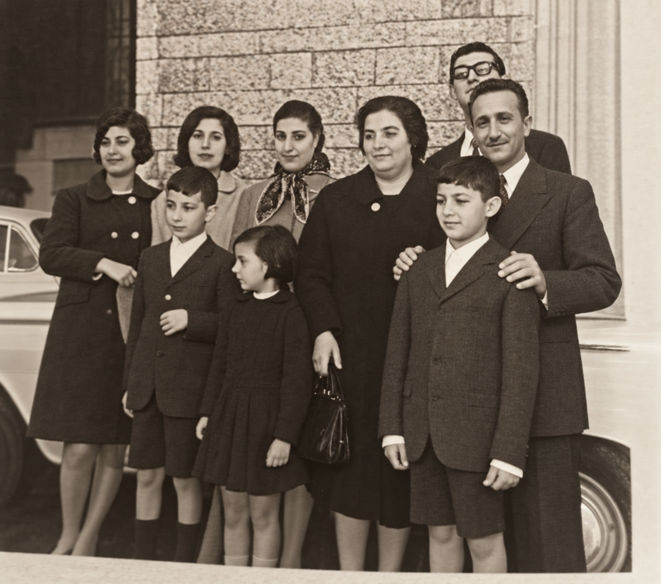Ritratto di un gruppo familiare con adulti e bambini davanti a un edificio.
