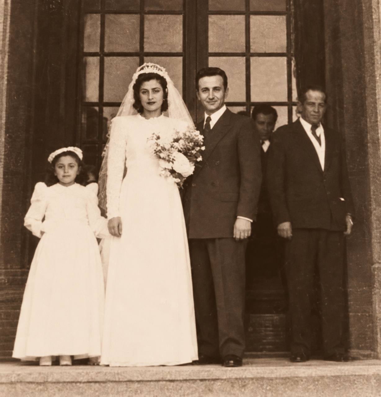 Ritratto di matrimonio: gli sposi davanti a un portone, con una bambina e due uomini.