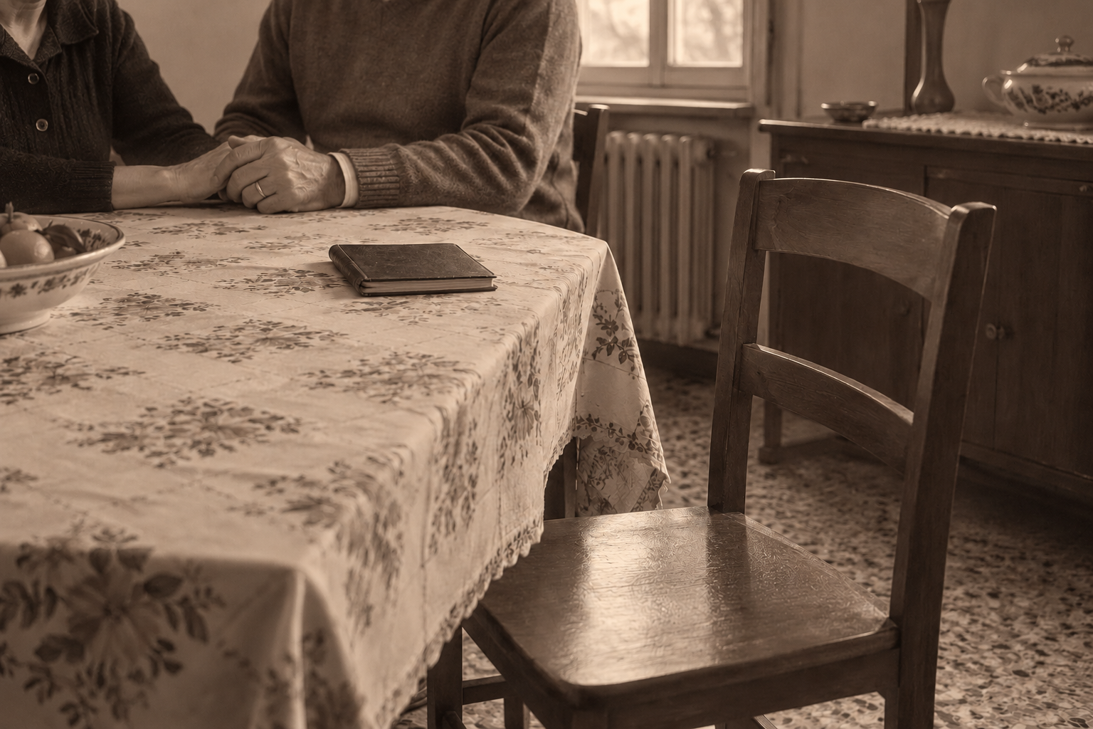 Una sedia vuota davanti alla tavola, con un libro chiuso e due persone sedute sullo sfondo.